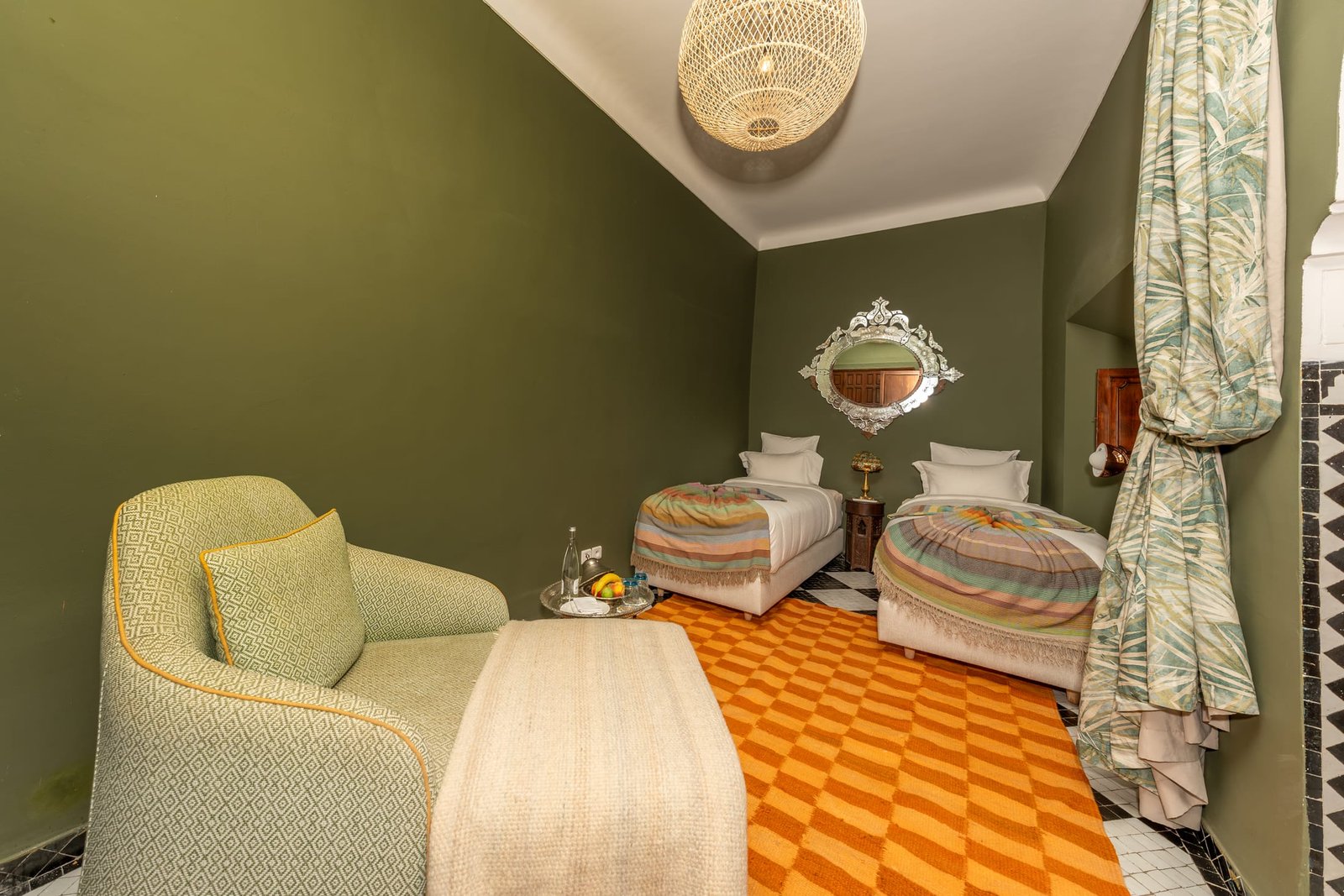 Une chambre verte à lits jumeaux, fauteuil et sol en carreaux orangés