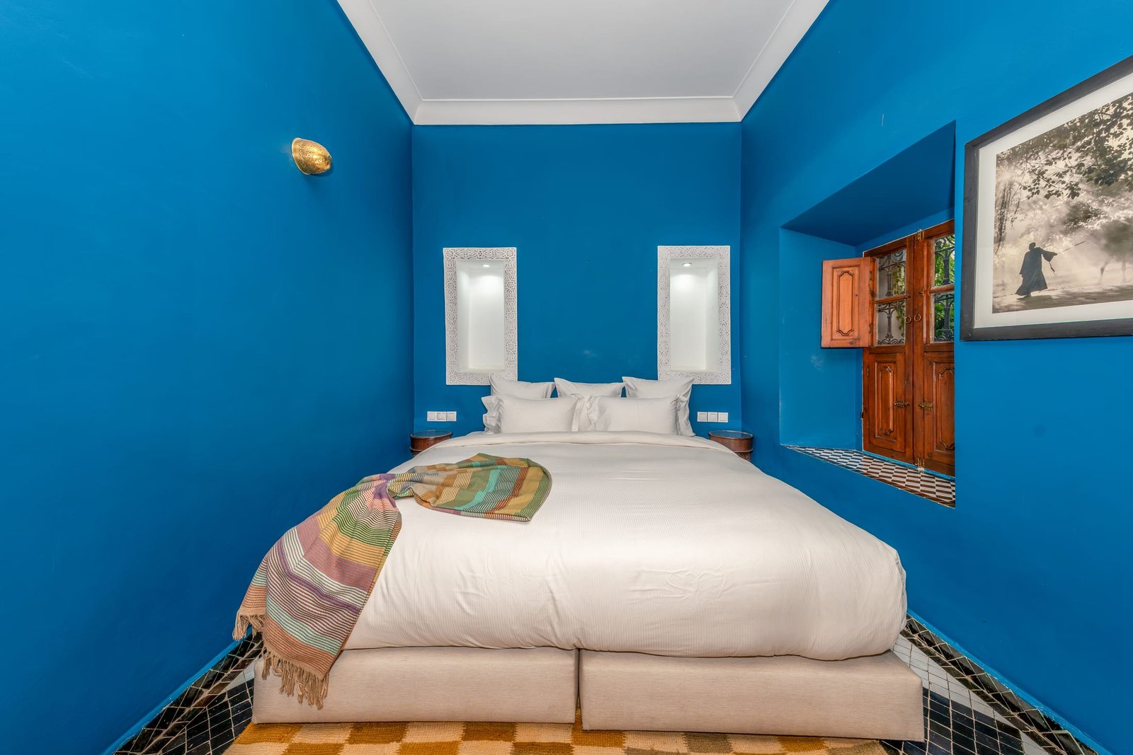Une chambre aux murs bleu vif, niches de plâtre blanc et fenêtre de cèdre sur le patio