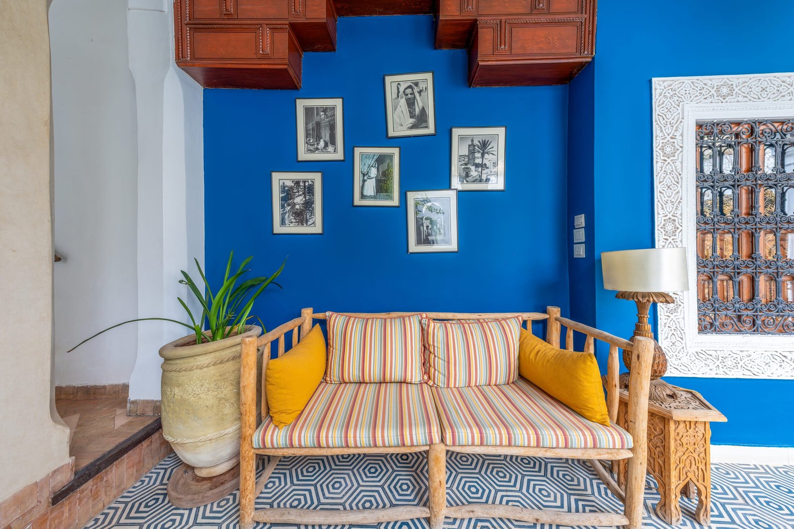 Un salon aux murs bleu vif, banquette de bois à coussins rayés et photographies encadrées