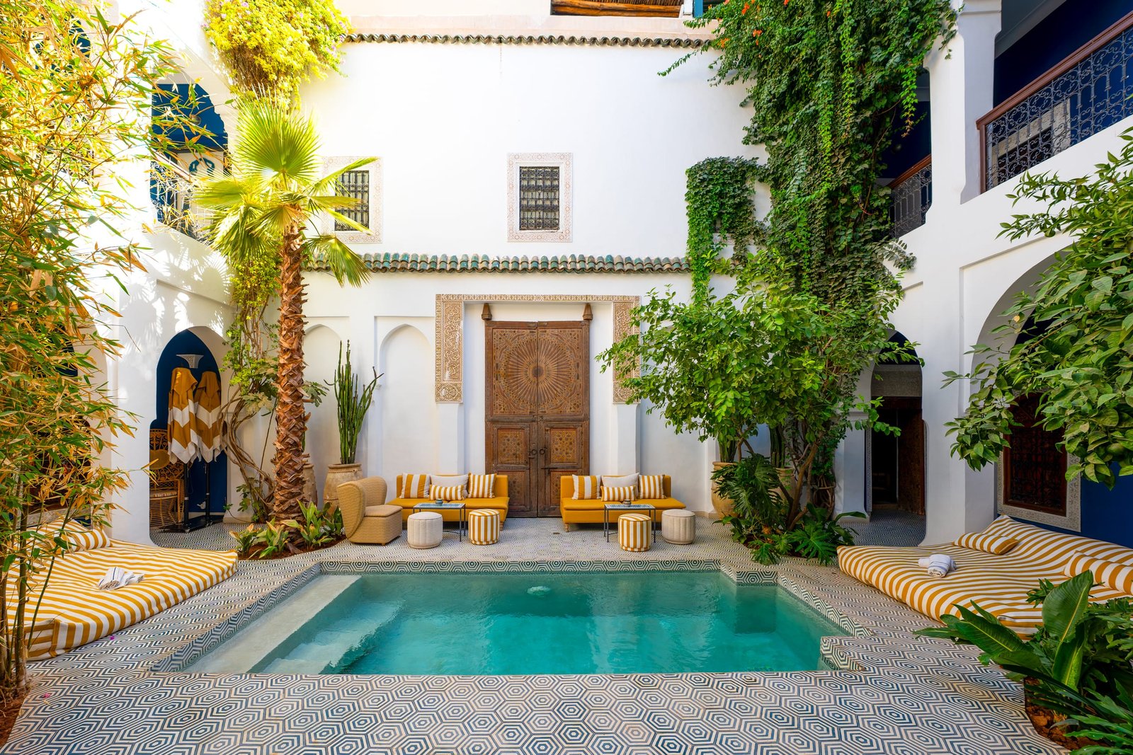 Le patio et son bassin, entre les orangers, avec une banquette rayée jaune et blanc au premier plan